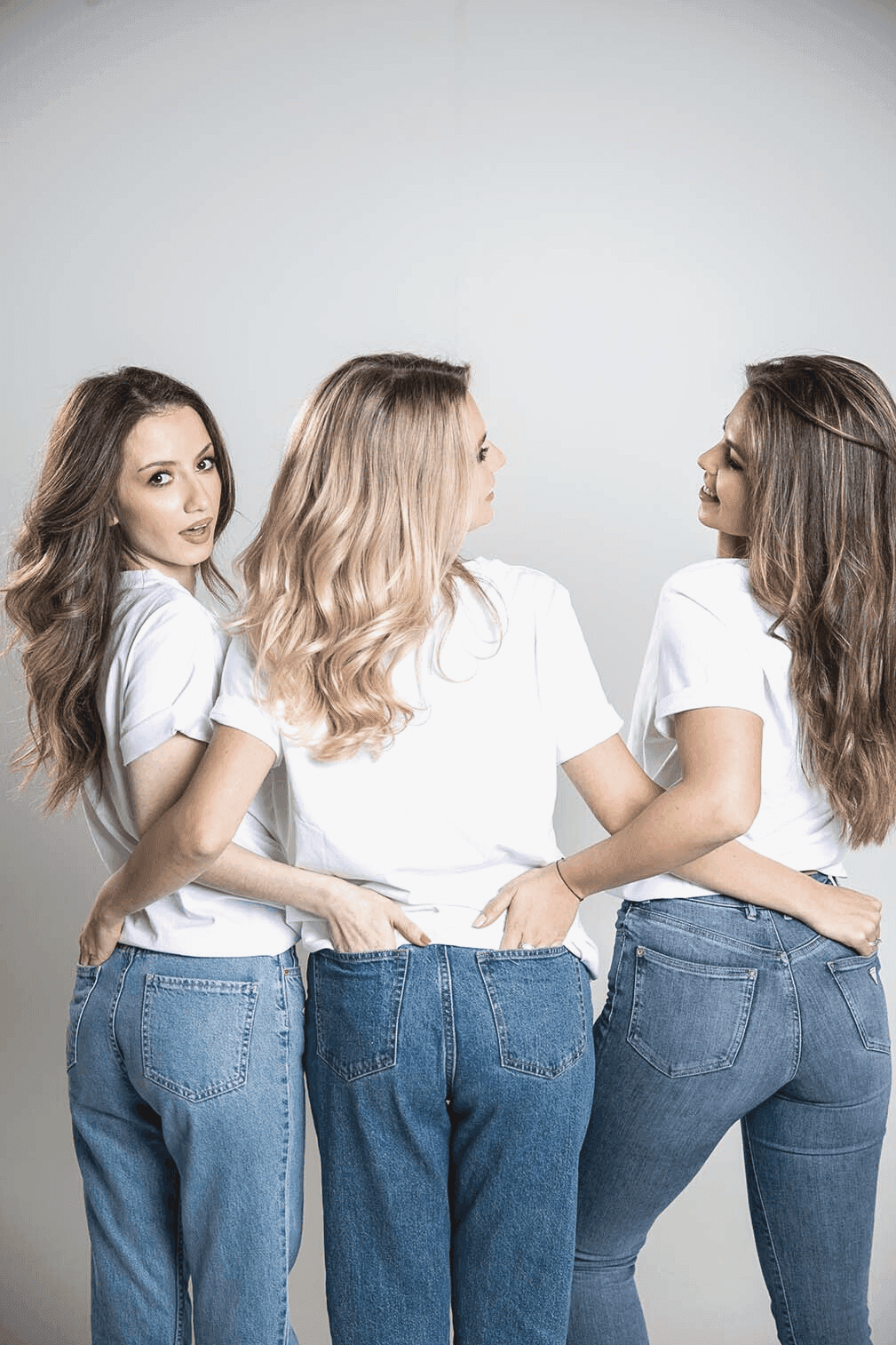 Trys merginos sėdi viena prie kitos